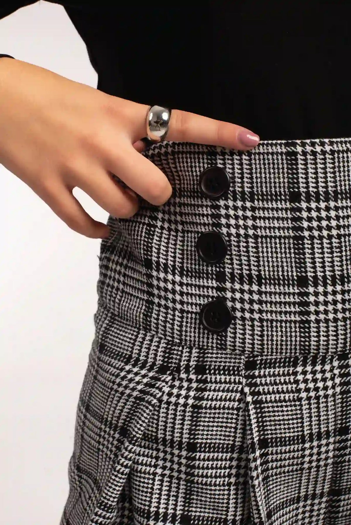 Silver dome ring worn on a hand beside the buttoned waistband of black-and-white plaid trousers, close-up