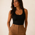 Black longline tank top tucked into camel trousers, three-quarter front view