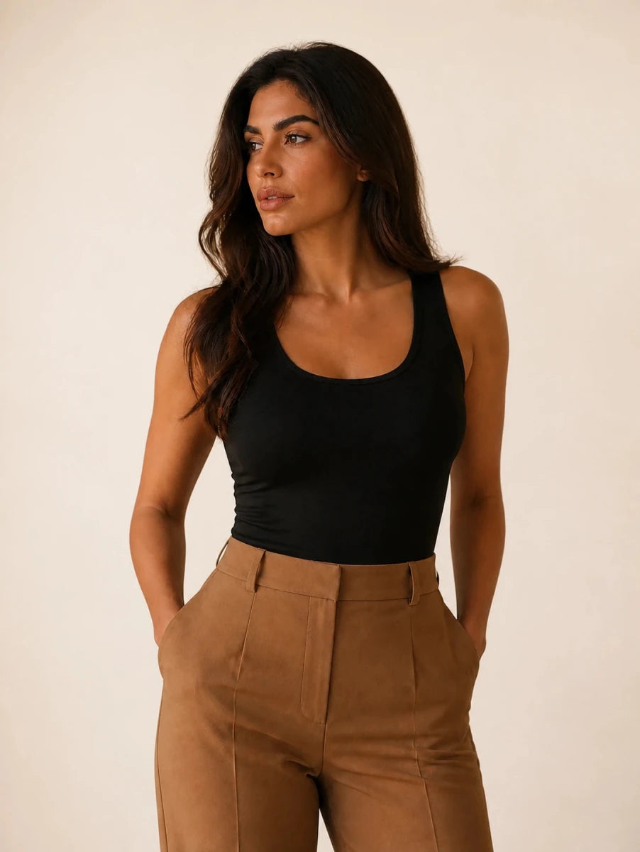Black longline tank top tucked into camel trousers, three-quarter front view